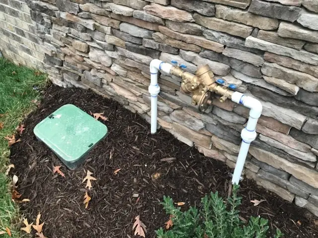 Backflow prevention and pressure valve assembly installed against a stone veneer foundation